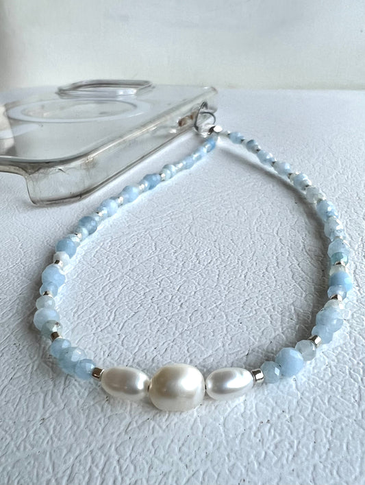 A pale blue phone wristlet made of faceted aquamarine stones and pearls.